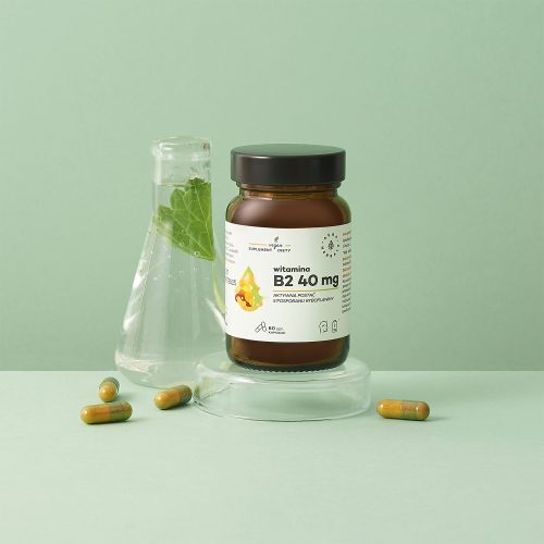 Brązowa butelka z etykietą Witamina B2 R-5-P 40 mg jest umieszczona na szklanym stojaku z zielonymi kapsułkami i szklaną kolbą zawierającą zielony liść, na jasnozielonym tle.