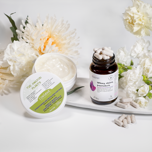 Zestaw aura herbals - zestaw 5-2 zawiera słoik kremu i otwartą butelkę kapsułek wyeksponowane na tacy z białymi kwiatami oraz kilka kapsułek rozrzuconych w pobliżu butelki.