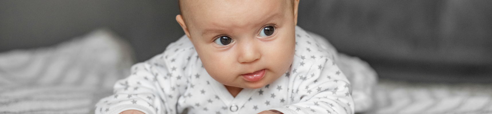 Urocze dziecko w wieku 6 miesięcy leży na kocyku w domu, patrząc przed siebie z szeroko otwartymi oczami i uśmiechem